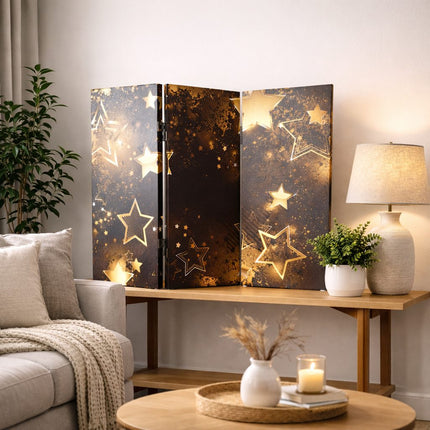 Stijlvol kamerscherm met goudkleurige sterren in een rustige woonkamer met houten meubel, grote lamp en plant.