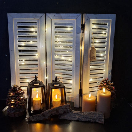 Wit houten shutters met kerstverlichting, dennenappels en warme kaarsen