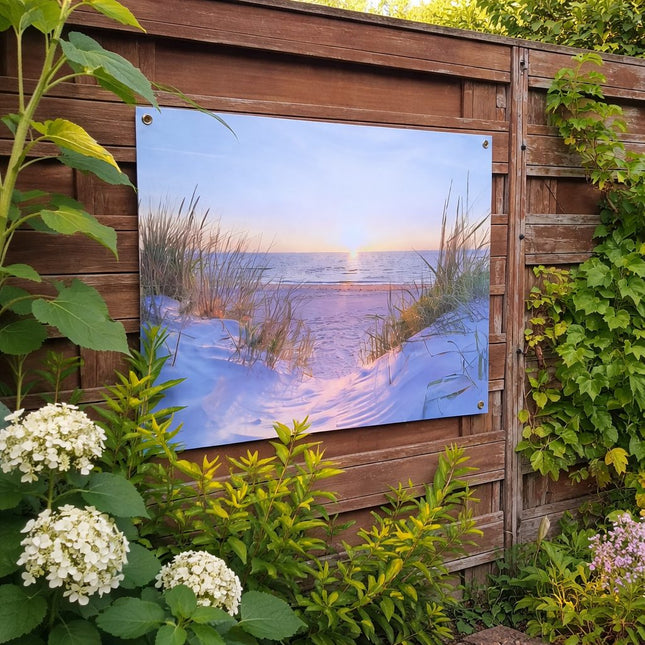 Sfeerfoto van tuinposter met strandduinen en zonsondergang, gemonteerd op houten schutting in een groene tuin